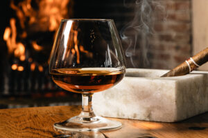 A brandy snifter and lit cigar resting on a marble ashtray beside a crackling fireplace at Lanzerac